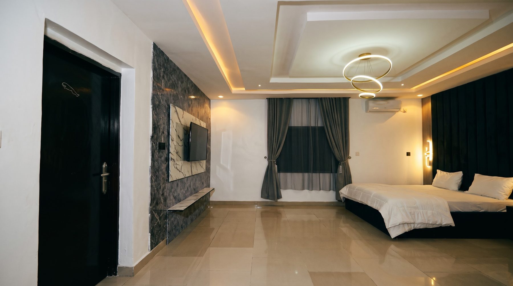 The Jaguar suite: bedroom with marble TV wall and ring chandelier, door with the Jaguar leaper on the left